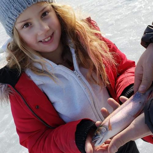 Young girl angler in a red winter coat hold a small trout
