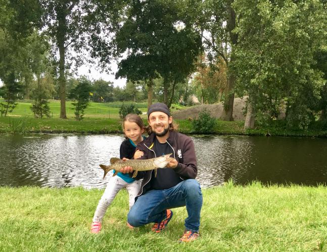 Father - daughter holding up a young norther pike on a summer day near the waters edge