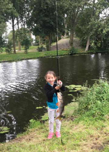 Small girl wih rod and reel at  edge of pond hold up her fish