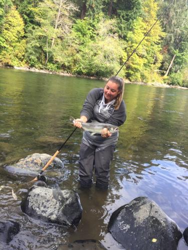 Lady fisher Fly Fishing knee deep in a stream hold up a nice trout