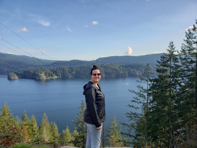 Lady hiker standing on a hill above a deep lake cove and forest beyond