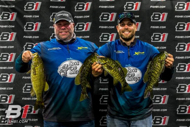 Two fishing tournament winnings holding up prized smallmouth bass after weigh in.