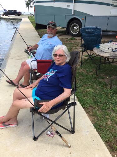 Man & women anglers fishing from a sidewalk next to the waters edge