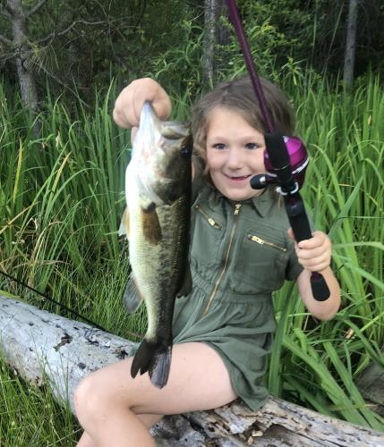 Young girl sitting on a log holding up a large bass