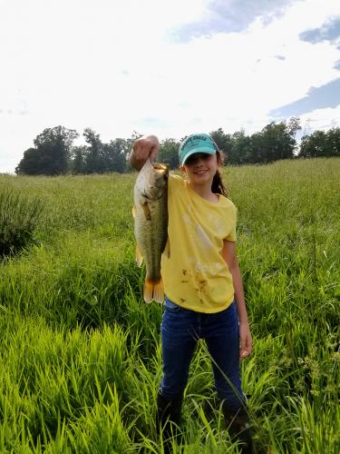 Girl angler standing in a field holding up a large bass