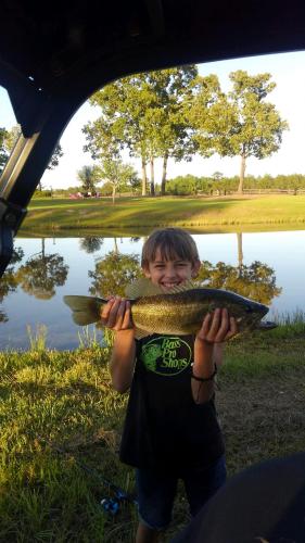 Boy angler pond fishing & holding a bass