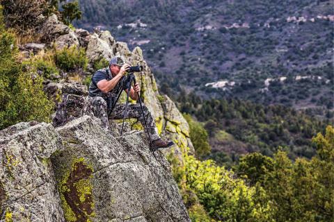 Hunter glassing with a spotting scope on a rock