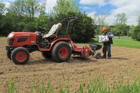 Land owner is loading seed spreader behind his tractor  to plant a food plot