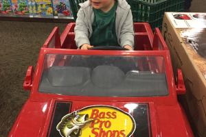 Toddler boy sitting in an electic bass pro chevy truck in toy section of a Bass Pro retal store.