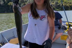 Young Abbigael standing in a boat holding up the fish she caught