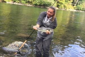 Lady fisher Fly Fishing knee deep in a stream hold up a nice trout
