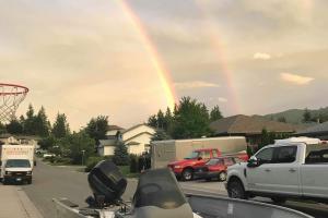 Boat parked on a street with a double rainbow in the sky