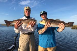 Grandfather and grandson holding up to redfish they caught in St. Bernard, LA