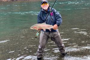 Angler standing in a stream showing off a beautiful steelhead trout