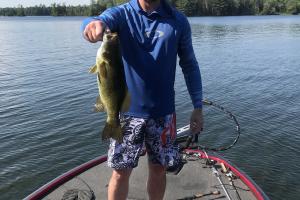 Bass fisher standing on a bass boat holding a large bass