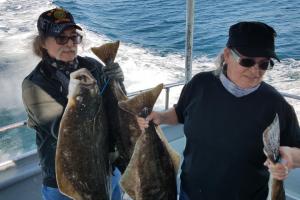 Two people holding several flounder