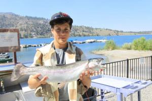 Young boy standing in front of a lake at a boat marina with a long rainbow trout