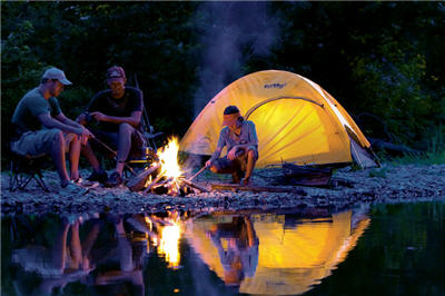 Campers on a river bank at night sitting next to a campfire