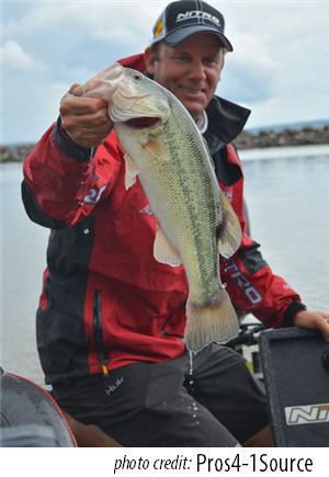 Pro angler Kevin VanDam sitting in a  boat holding a largemouth bass