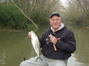 Angler sitting in a small boat holding up a fish with a spinning rod and reel