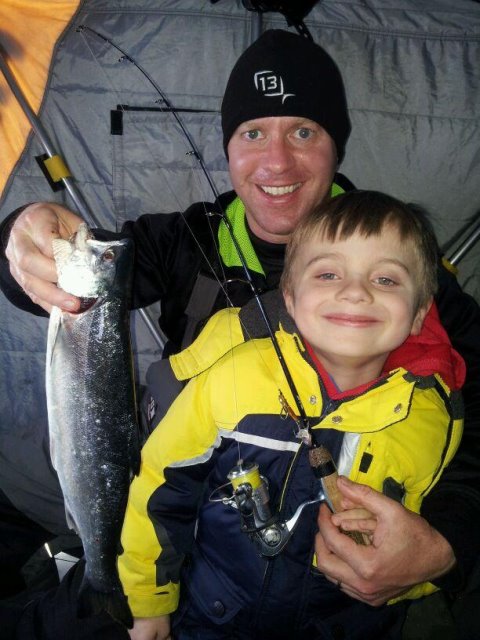 Man and young boy in ice shelter holding fish and ice fishing rod