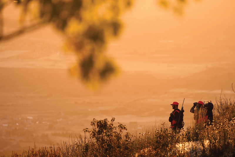 two hunters standing on ridge at sunset