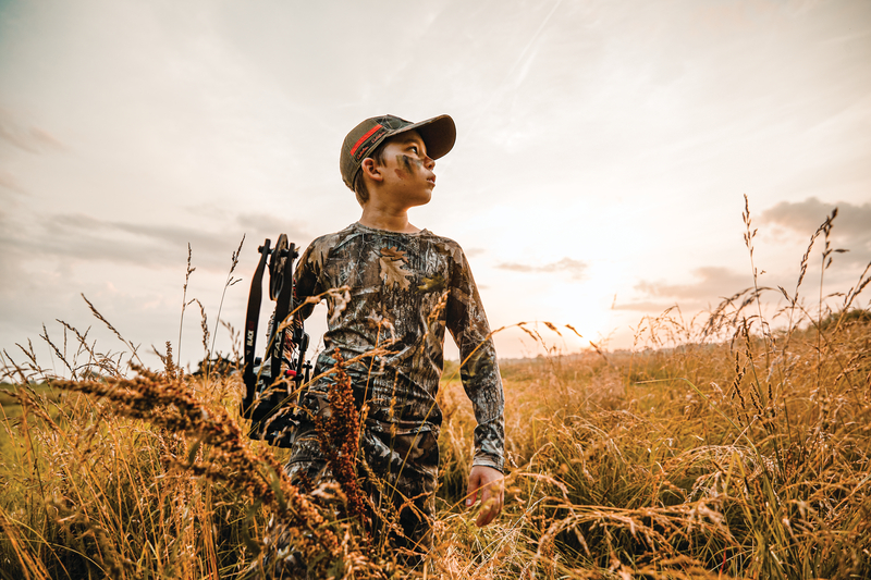 Youth archer walking through field with bow in hand