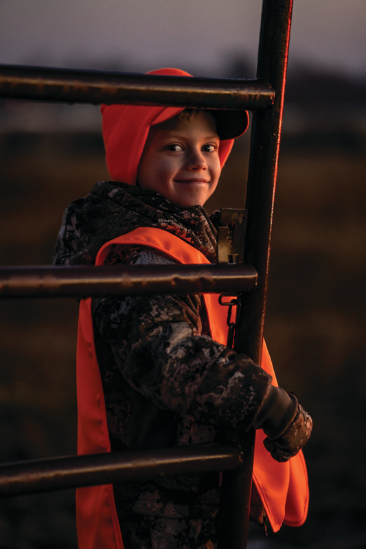 Young hunter in blaze orange and camo next to stand ladder