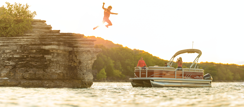 Man jumps from cliff into water with boaters watching