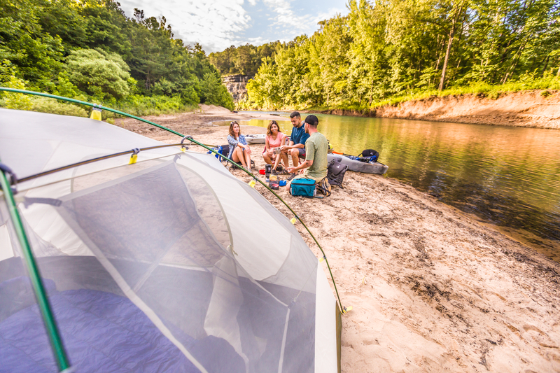 campers eating lunch next to river with kayak on shore