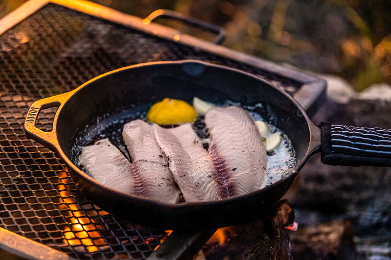 cooking fish fillets on cast iron skillet over camp fire