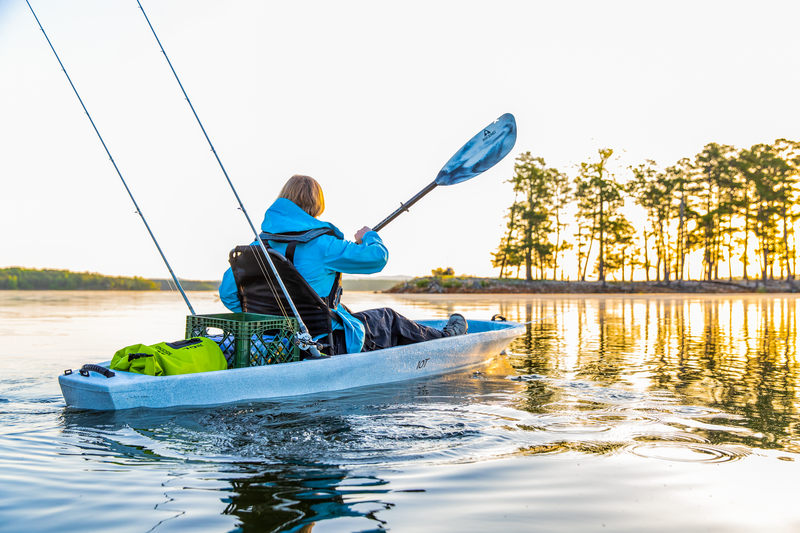 kayaker with fishing gear paddling across lake
