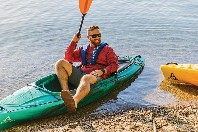 man leaning back in ascend kayak at shore