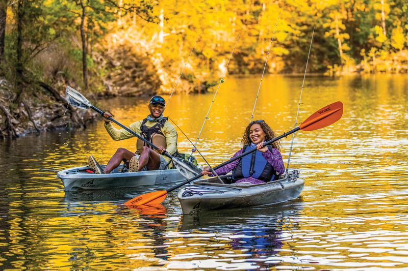 two kayakers paddling down river with fishing gear