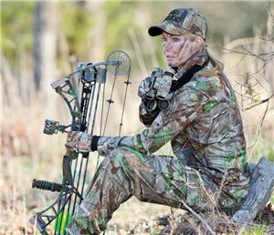 Female bowhunter sitting next to tree with her compound bow