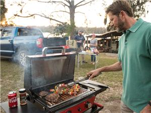 Man staning at an outdoor grill at a campsite grilling meat and vegitables
