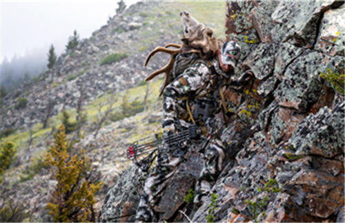 Deer hunter climbing up rocks with a buck's head strapped to his back