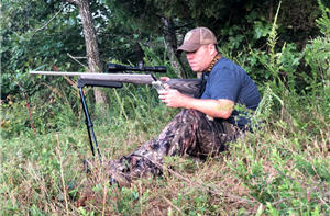 Coyote hunter sitting edge of woods with rifle