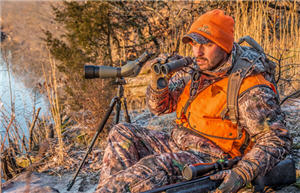 Deer hunter sitting on a rocky ridge scouting the water and land for a whitetail