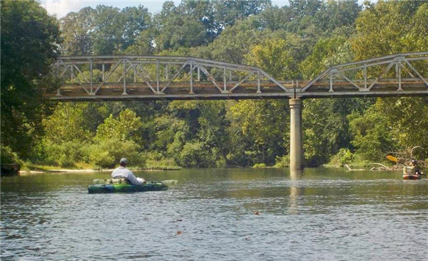 Two people in kayaks floating a river in Missouri towards a bridge crossing