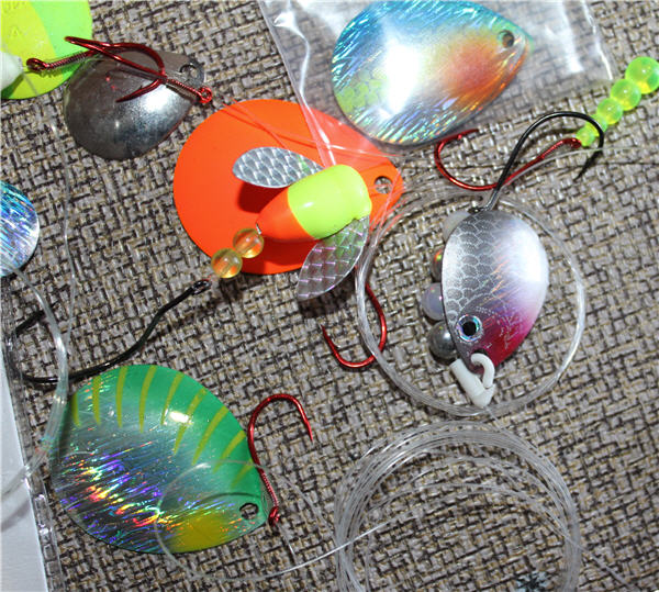 Several spinner blade colors, orange, green, metalic silver laying on table rigged with hooks