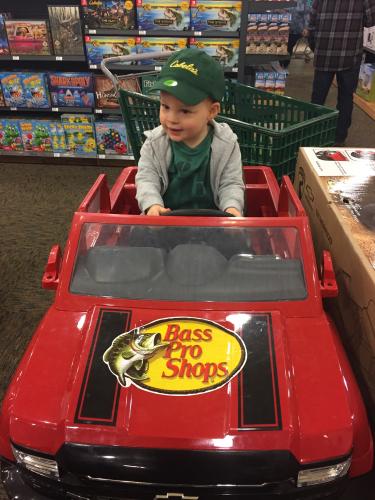 Toddler boy sitting in an electic bass pro chevy truck in toy section of a Bass Pro retal store.