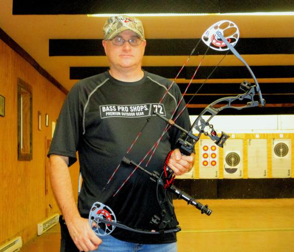 Archer at an inside archery range holding up his compound bow to see
