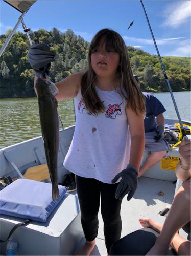 Young Abbigael standing in a boat holding up the fish she caught