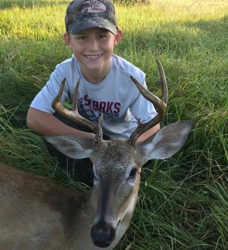 Young boy deer hunter sitting near his buck harvest