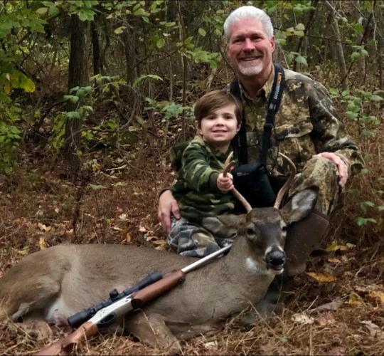 Deer hunter posing with deer and young son