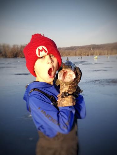 Young ice angler holding an open mouthed fish with his mouth open too