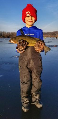 Boy standing on frozen lake hold up the fish he caught ice fishing