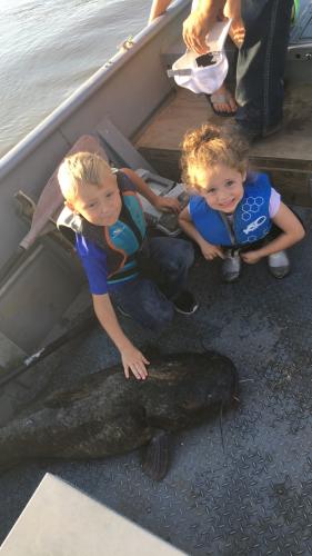 2 children in a boat petting a blue catfish