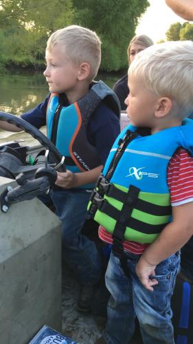 Young boy driving a boat with another young boy watching